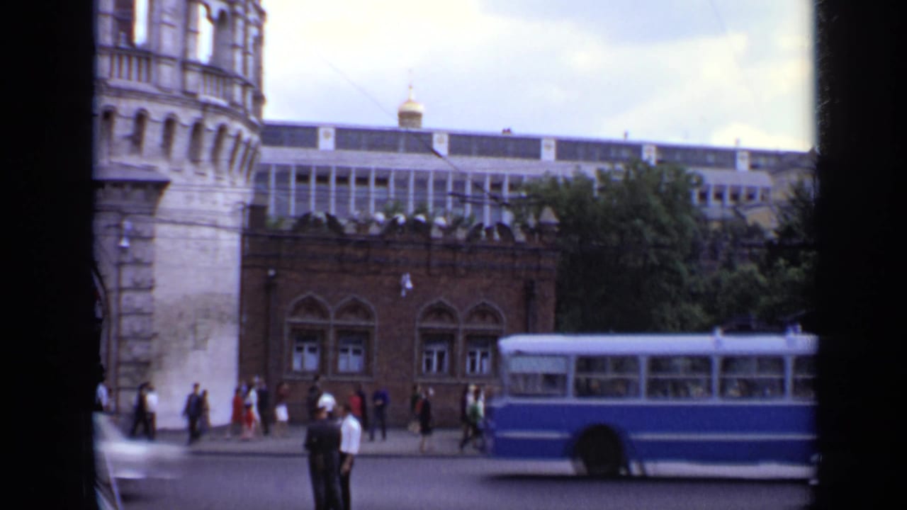 Moscow street with pedestrians, a blue bus, a stone tower, and arched windows.
