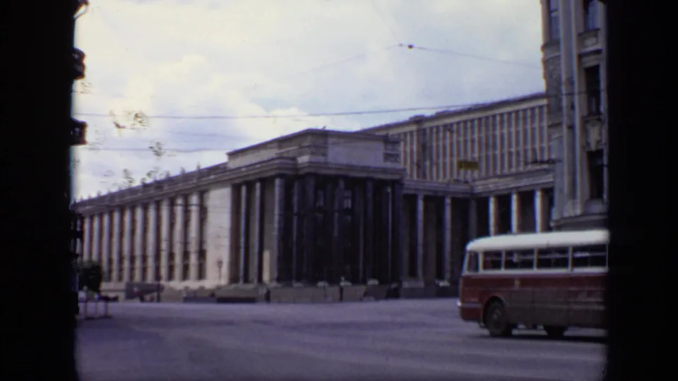 1971 Moscow street scene showing a long columned building, overhead wires, and a red-and-white bus along the roadway.