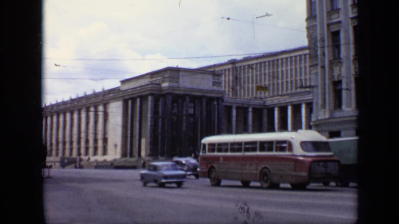 1971 Moscow street traffic passes in front of a monumental columned building, with a bus, cars, and overhead wires visible.