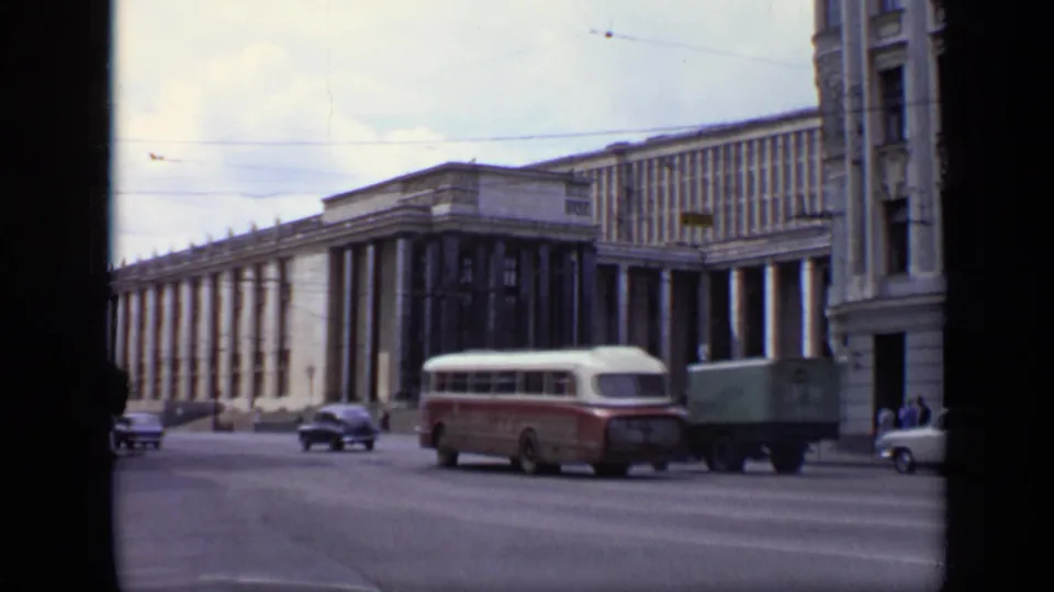A 1971 Moscow street view shows a red-and-white bus, small truck, and cars moving past a large columned building.