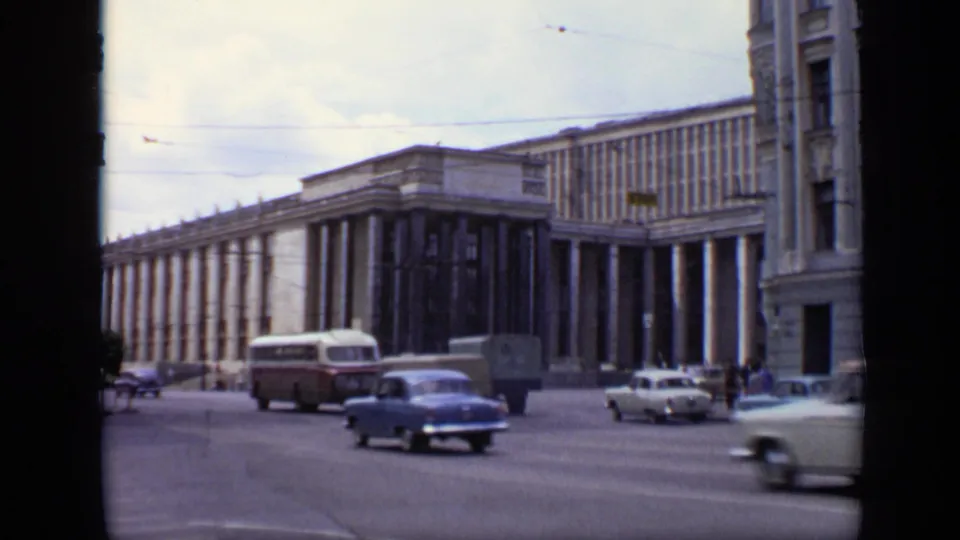 1971 Moscow traffic fills the foreground as cars and a bus pass a large columned building, with pedestrians faintly visible near the curb.