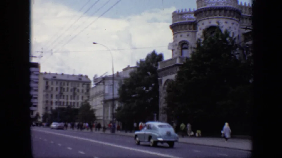 1971 Moscow boulevard with a light blue sedan, pedestrians, overhead wires, trees, and a mix of older facades and taller modern buildings.
