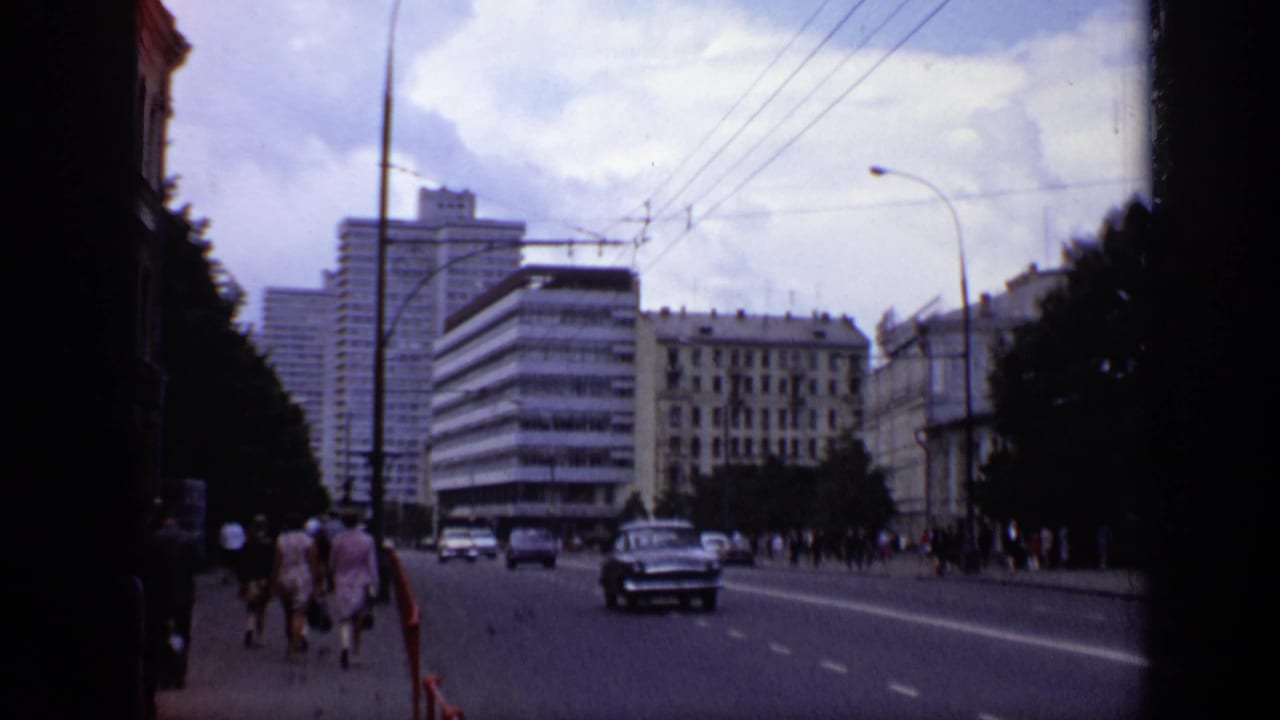 City street with cars, pedestrians, tall buildings, trees, and power lines.