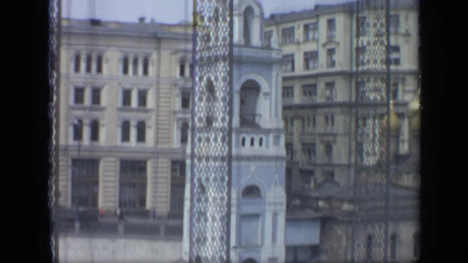 Moscow buildings and a pale church facade viewed through patterned window screening, with soft 8mm grain and muted color.