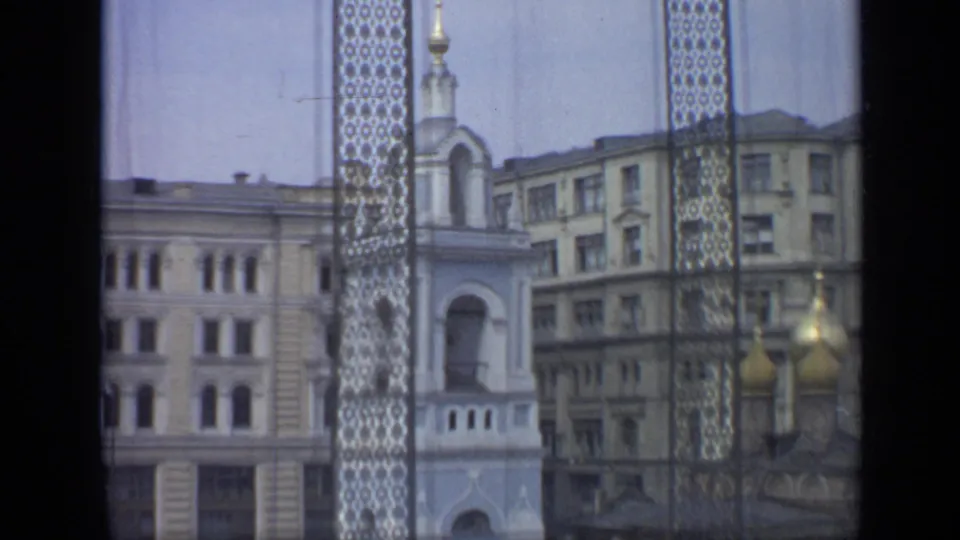 1971 Moscow view through patterned screening toward a church facade, surrounding buildings, and golden domes partly visible at the lower right.