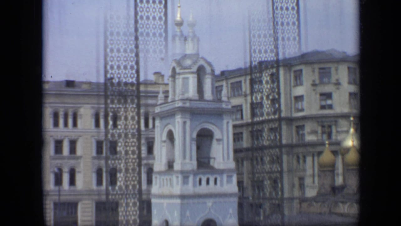 White bell tower and golden domes seen through a patterned metal grille.