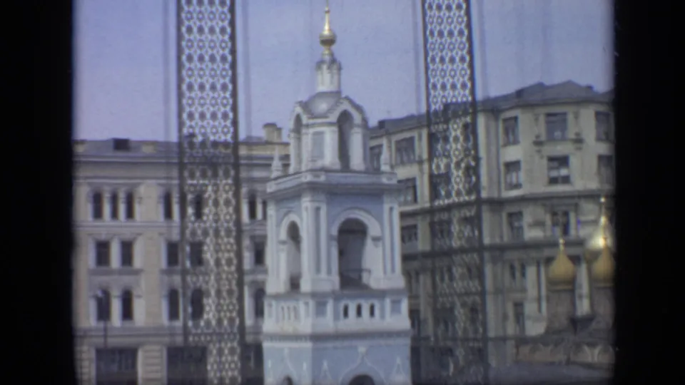 1971 Moscow frame with a white tower centered behind a decorative grille, with golden domes and residential blocks nearby.