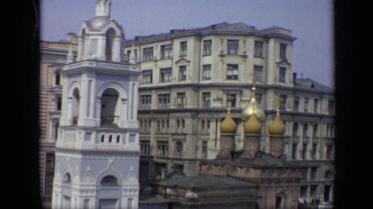 Golden onion domes and a white bell tower seen above city buildings.