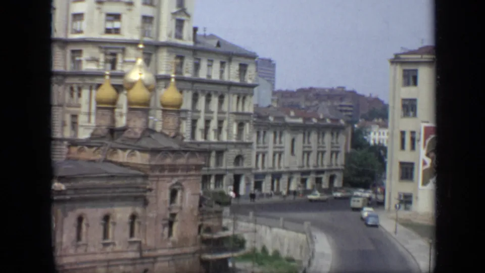 1971 Moscow street view from above, with church domes in the foreground, apartment buildings, cars, pedestrians, and a partial graphic sign.