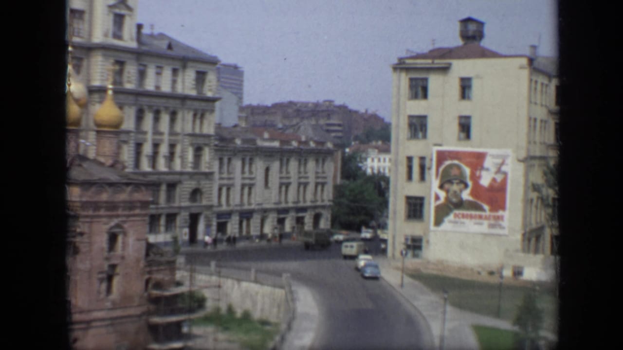 1971 Moscow view with a domed church partly at left, pale apartment blocks, light traffic, pedestrians, and a prominent Soviet soldier poster.