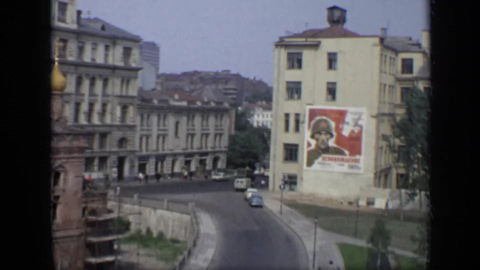 1971 Moscow street view with Soviet-era apartment buildings, a large soldier poster, vintage cars, small pedestrian figures, and a church edge at left.