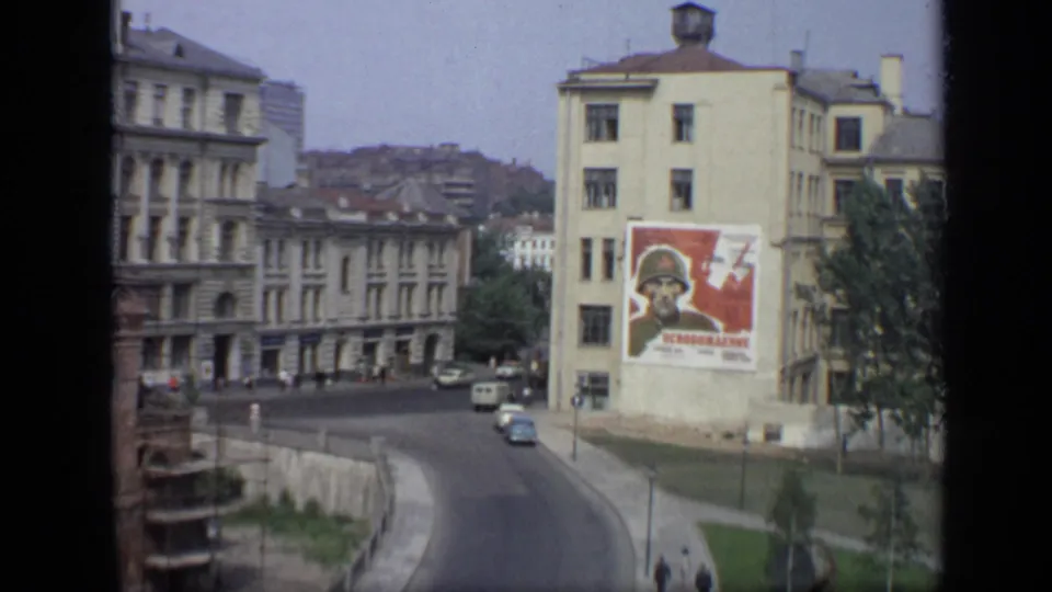 1971 Moscow street scene showing a political soldier poster on a facade, Soviet-era buildings, light traffic, pedestrians, and trees at the edge.