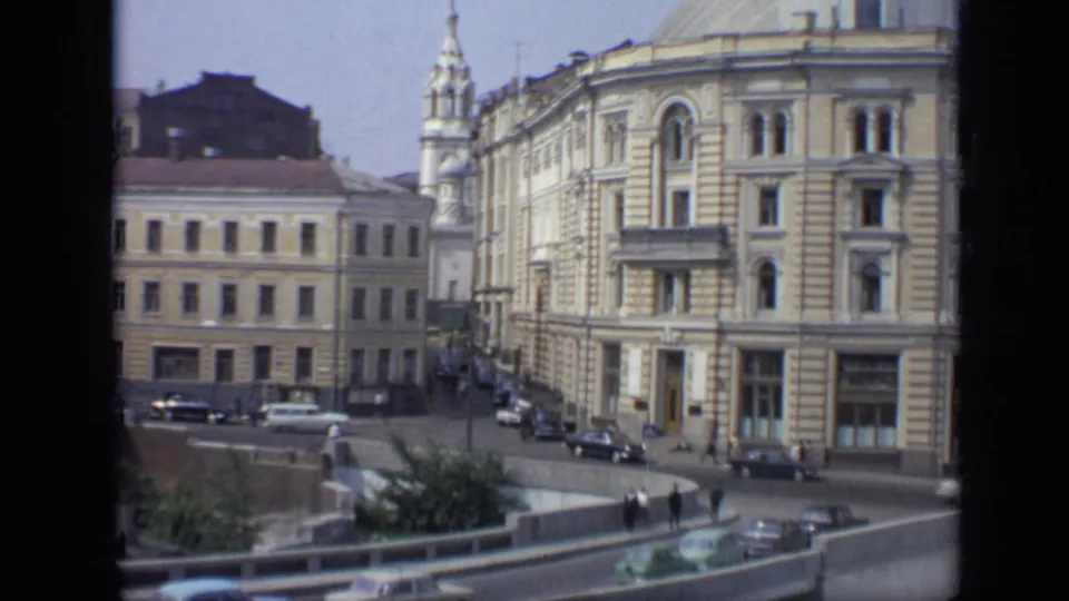 1971 Moscow street scene showing ornate masonry buildings, a church spire, period vehicles, pedestrians, and a curved roadside barrier.