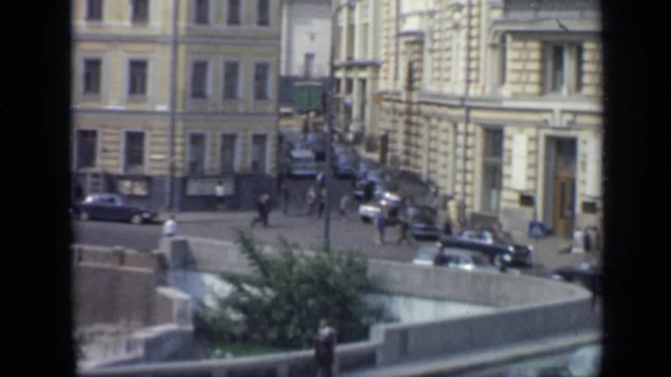 1971 Moscow street corner with pedestrians, classic cars, a planted concrete island, and ornate building facades.
