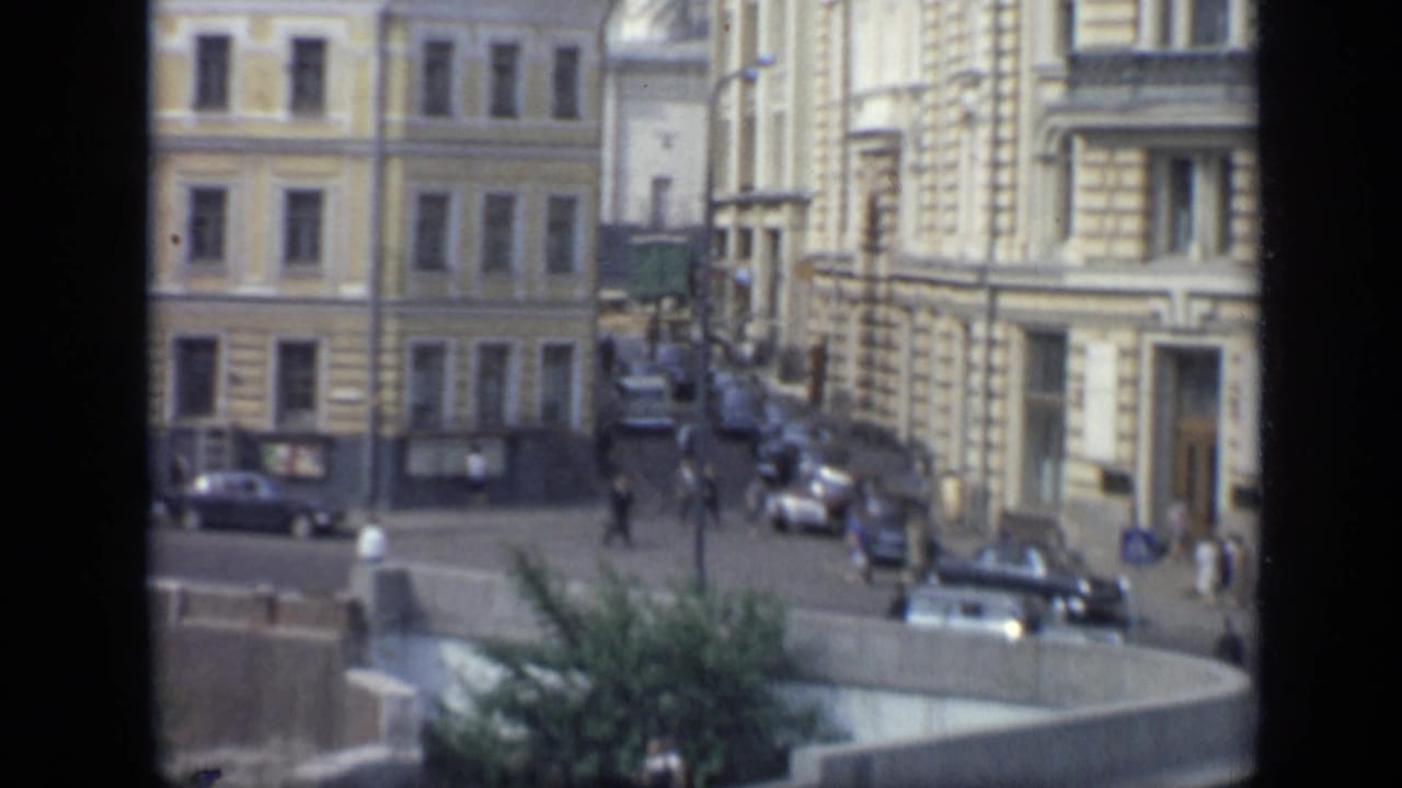 1971 Moscow street view with masonry facades, parked cars, pedestrians, sidewalks, and a home-movie frame edge.