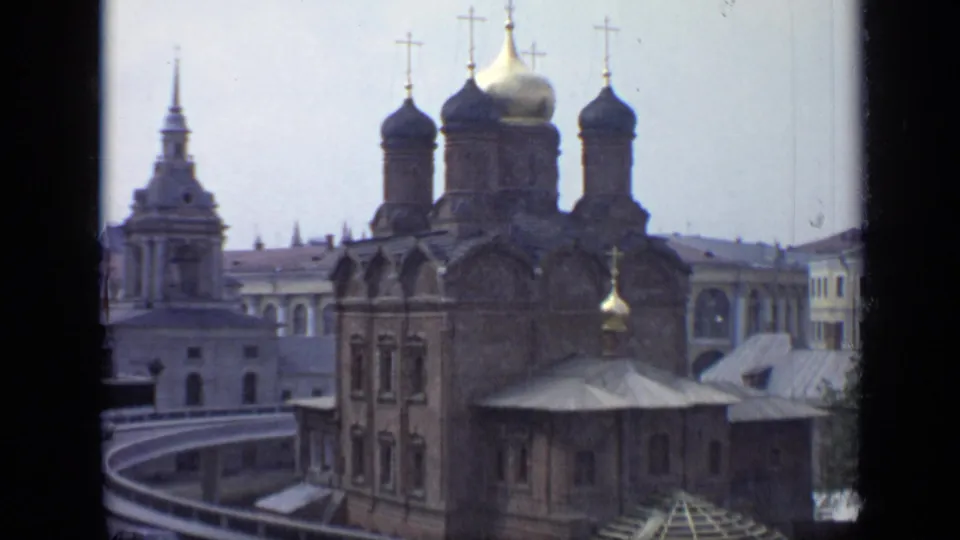 1971 Moscow 8mm frame showing a Russian Orthodox church facade, onion domes, gold cross, pale tower, rooflines, and road curve.