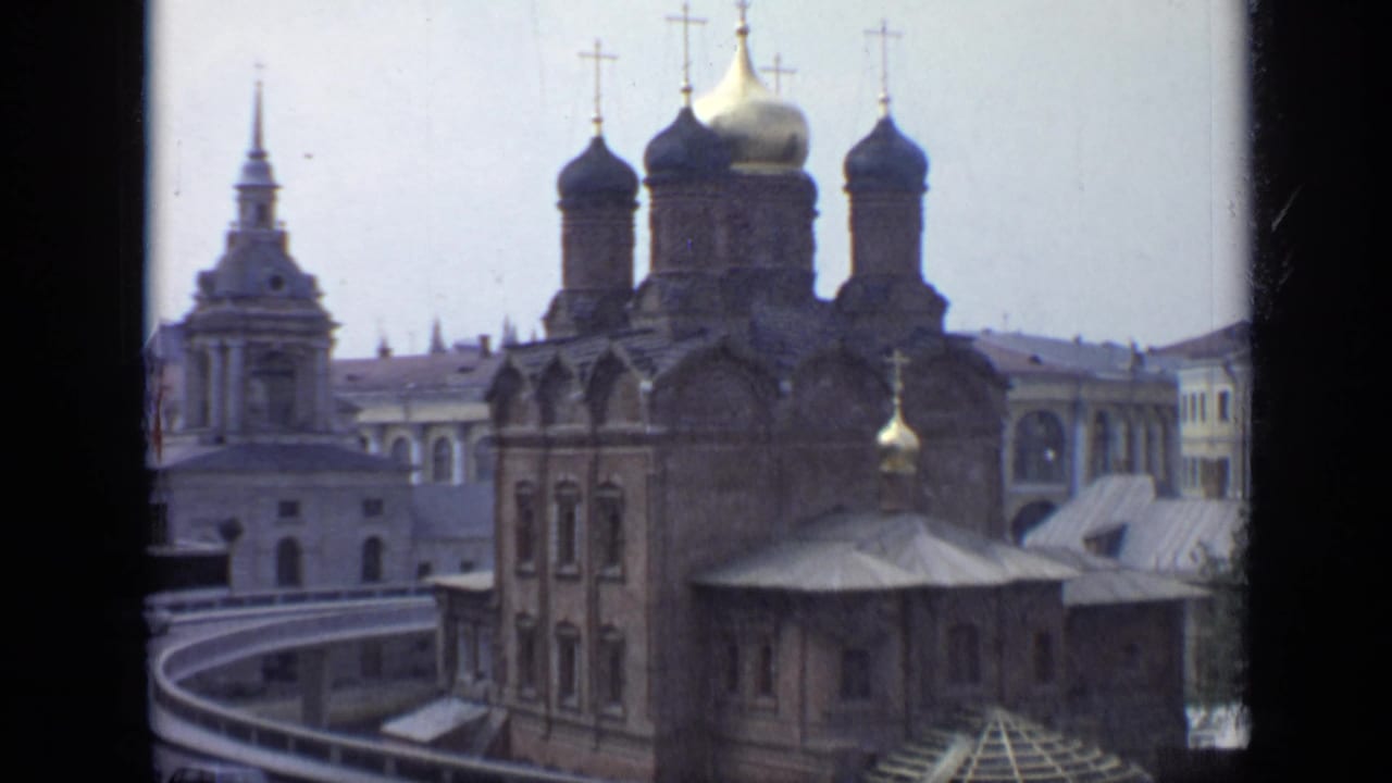1971 Moscow 8mm frame showing a brick Orthodox cathedral with onion domes, crosses, and a neighboring tower under pale sky.