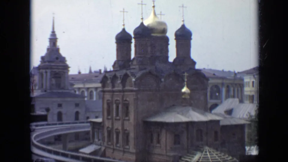 1971 Moscow 8mm frame showing a brick Orthodox cathedral with onion domes, crosses, and a neighboring tower under pale sky.