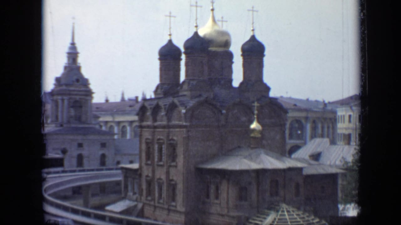 1971 Moscow 8mm frame with the cathedral centered, onion domes rising above brick walls and pale urban buildings.