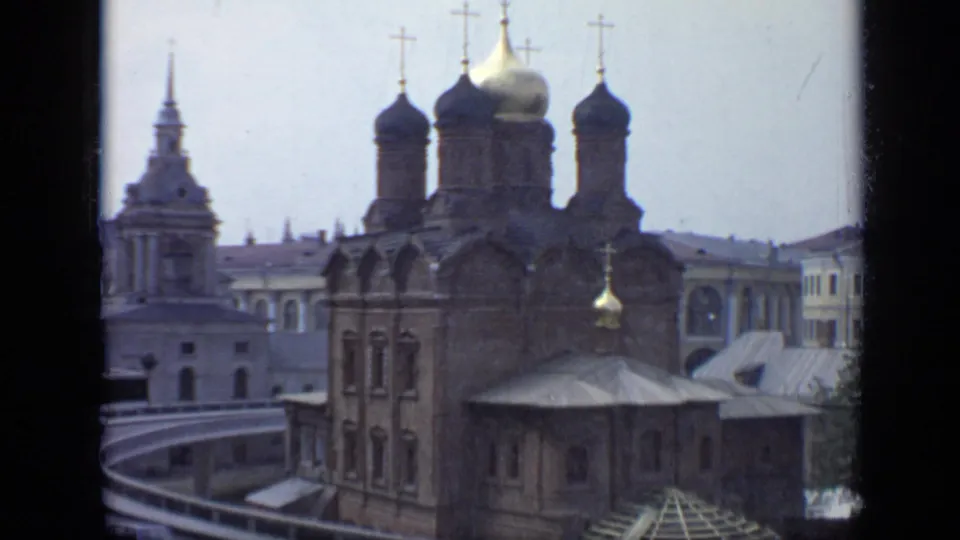 1971 Moscow home-movie frame showing a brick cathedral with dark onion domes and a smaller foreground roof.