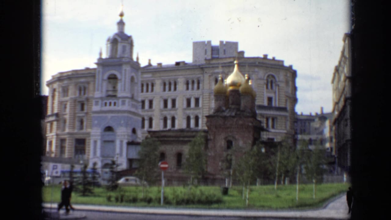 1971 Moscow street view with a small golden-domed church in front of a large Soviet-era urban building and pedestrians crossing nearby.