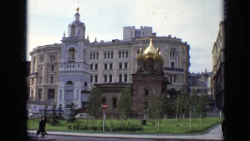 1971 Moscow street view with a small golden-domed church in front of a large Soviet-era urban building and pedestrians crossing nearby.