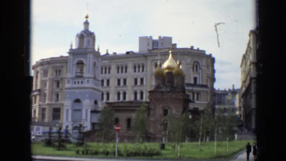 1971 Moscow frame showing a golden-domed church, a tall bell-tower feature on a nearby building, planted grass, signs, and distant pedestrians.