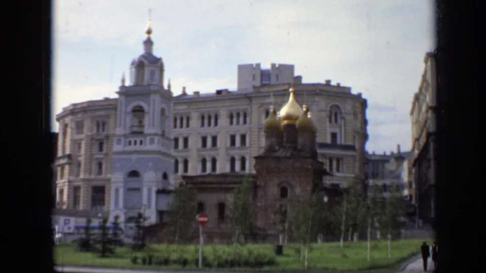 1971 Moscow 8mm frame with a small golden-domed church, broad urban facade, street signs, greenery, and partial pedestrians at the edge.