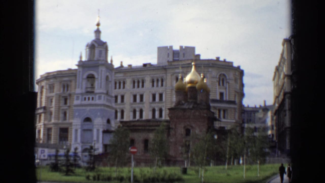1971 Moscow view of a white bell tower, golden-domed church, grass, and surrounding city buildings seen through a window edge.