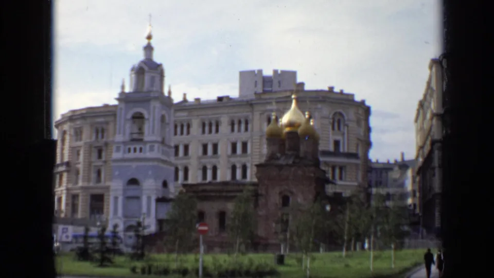 1971 Moscow view of a white bell tower, golden-domed church, grass, and surrounding city buildings seen through a window edge.