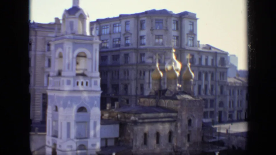 1971 Moscow shot holding on a white bell tower and golden onion domes, with a broad urban facade in the background.