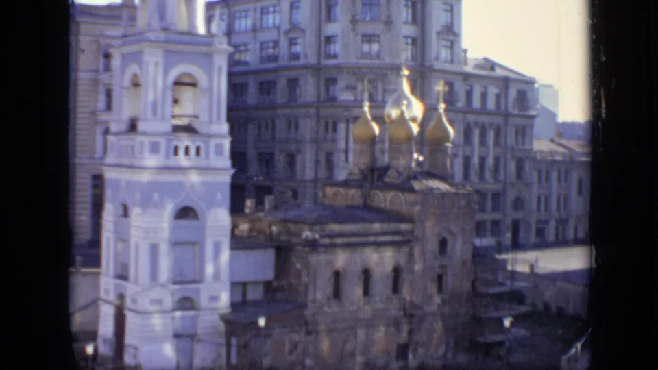 1971 Moscow frame showing golden church domes, a white bell tower, and dense city architecture through a dark window edge.