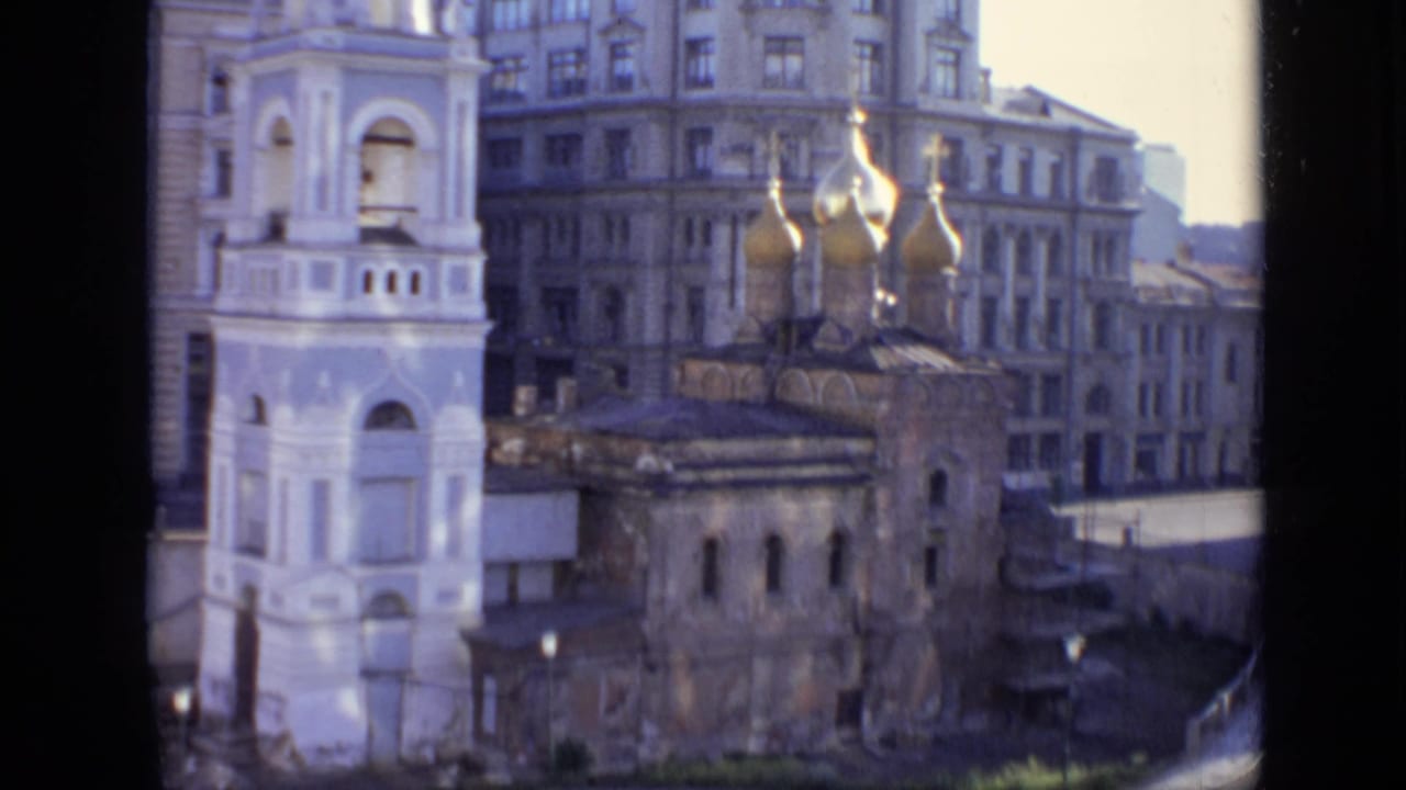 White bell tower and onion-domed church beside older city buildings.