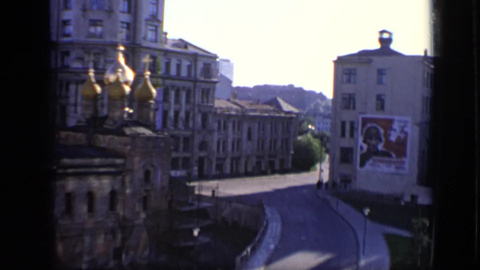 Elevated 1971 Moscow view showing church domes in the foreground, a quiet street, older buildings, and a large political-looking wall poster.