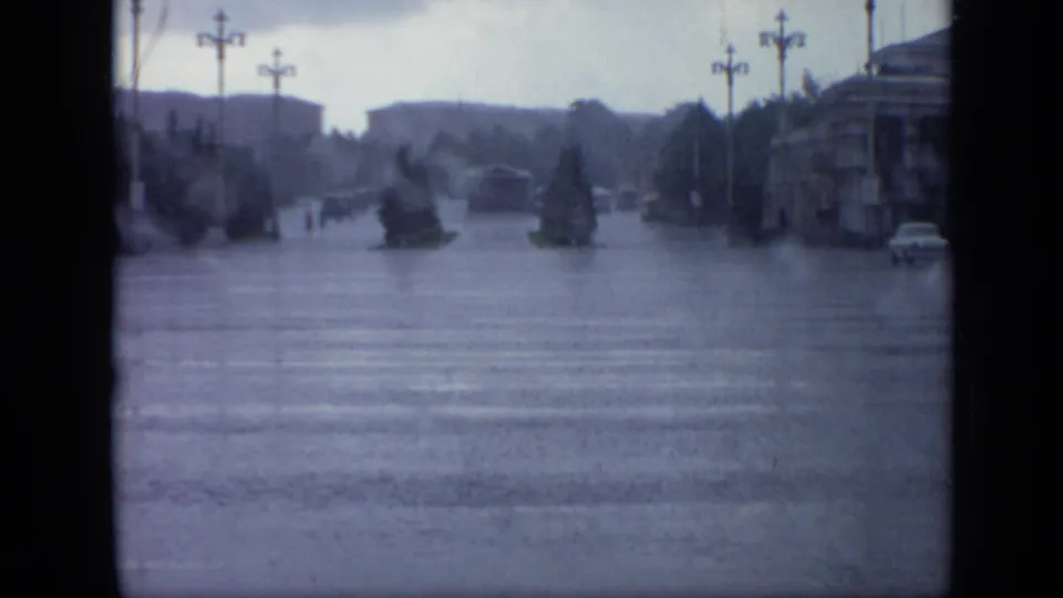1971 Moscow rain scene showing a flooded broad street, crosswalk, planted islands, distant people, older lamps, and a corner building.