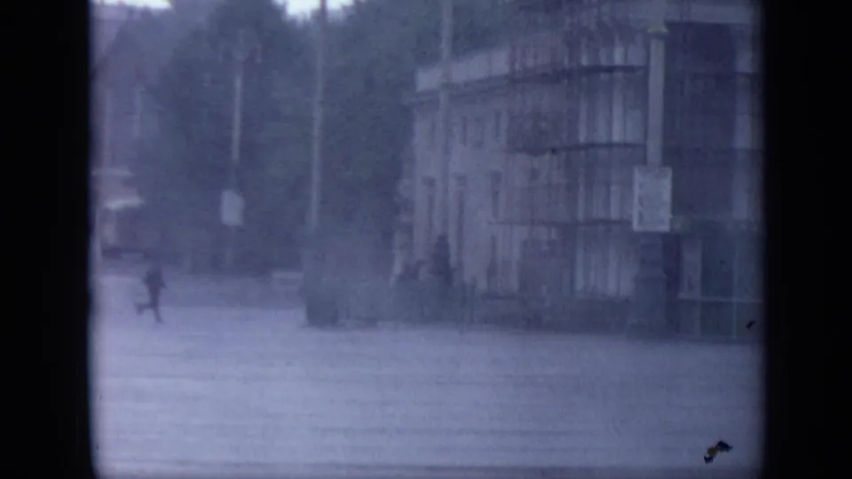 1971 Moscow frame with pedestrians crossing wet pavement in heavy rain beside a large public-looking building facade.