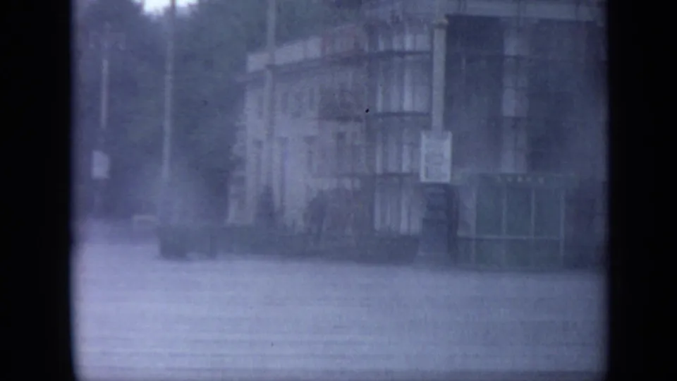 Soft 8mm view of a rain-soaked Moscow building area in 1971, with wet pavement and a large facade softened by weather and film texture.