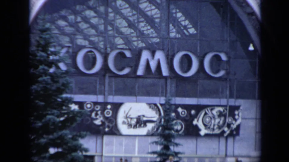 1971 Moscow exterior of a building facade with large Cyrillic KOSMOS lettering, glass panels, trees, and a graphic banner below the sign.