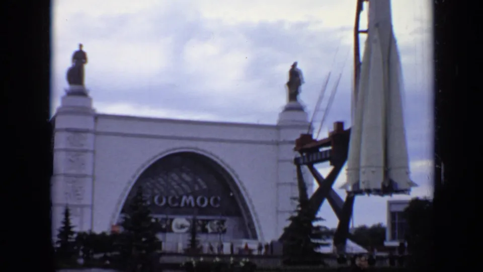 1971 Moscow frame with the Kosmos pavilion in the background and a rocket mock-up on a gantry at right under a cloudy sky.