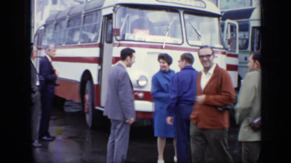 Close view of adults talking beside a white-and-red bus in 1971 Moscow, with rain-darkened pavement underfoot.