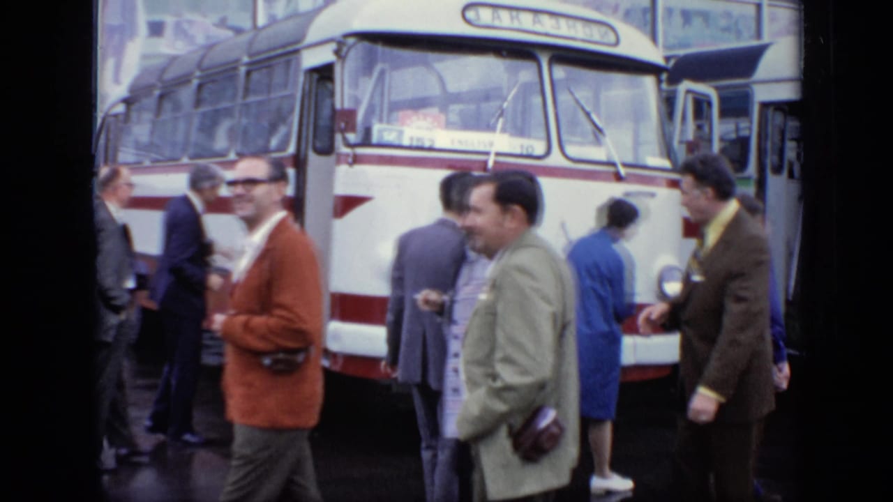 1971 Moscow 8mm frame showing adults in coats and suits near a red-and-white bus on wet pavement.