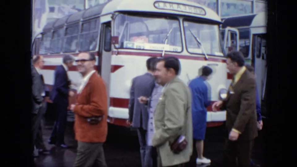 1971 Moscow 8mm frame showing adults in coats and suits near a red-and-white bus on wet pavement.