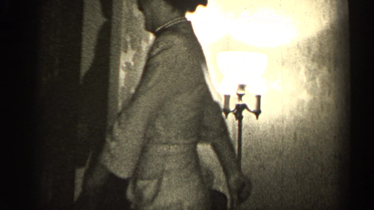 Woman in a dress turns in profile near a lit standing lamp.