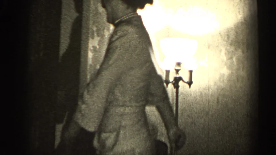 The woman appears in profile near a bright lamp, her dress and posture emphasized by the high-contrast 8mm exposure.