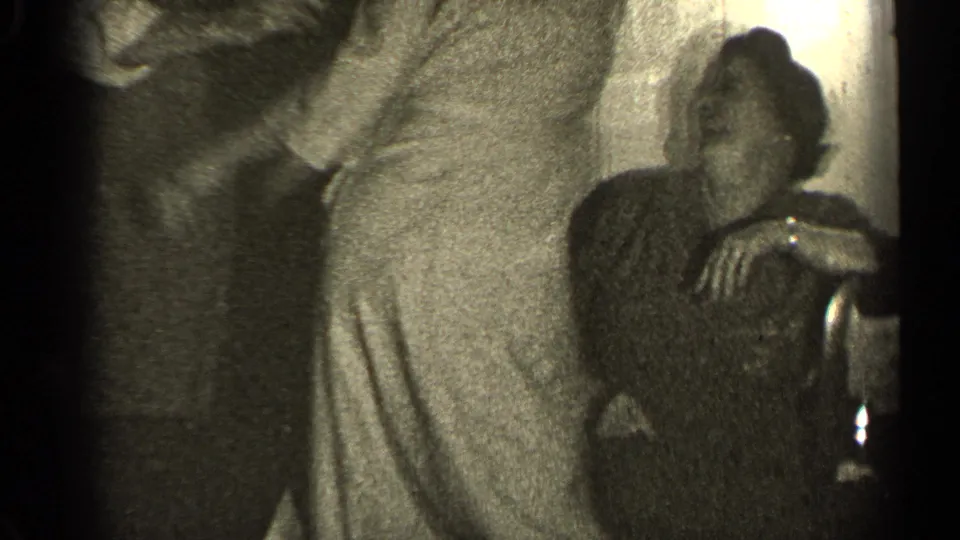 In the private interior, the woman leans toward a man in a suit jacket as the scene shifts from posing to affectionate contact.