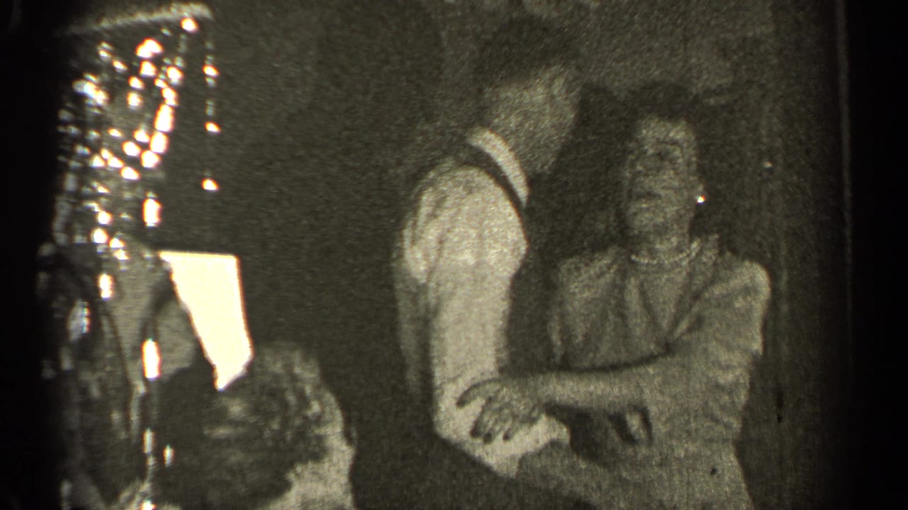Couple dancing indoors with seated guests and bright background light.