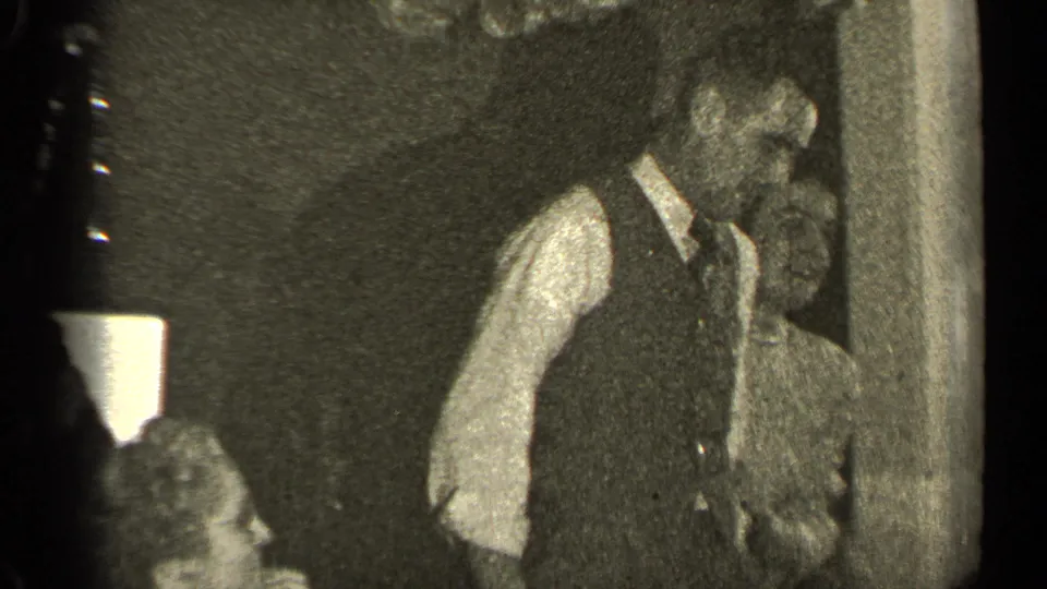 A man in a dark vest and tie dances with a woman in a light dress at an Illinois indoor gathering.