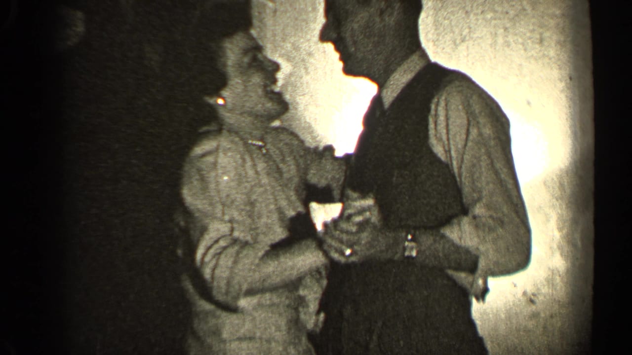 Adult couple dances closely in a dim interior, with the man in a vest and tie.