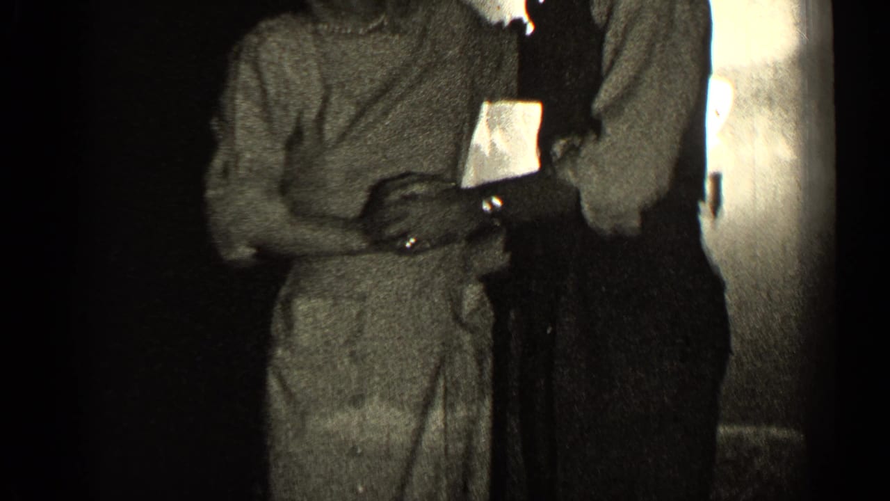Two adults stand close together while dancing near a doorway or wall.