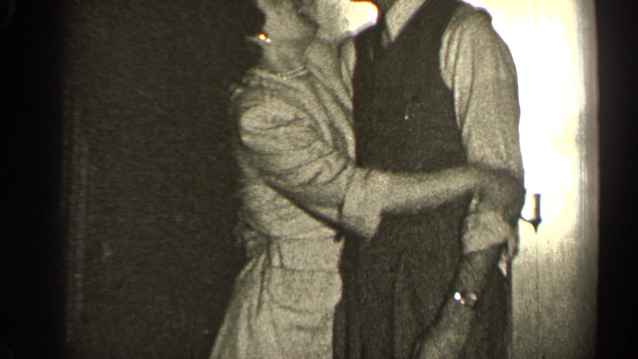 Couple standing close indoors, embracing and kissing near a doorway.